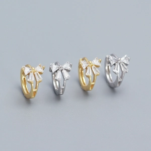 Detail of bow-shaped stud earrings in gold and silver finish with sparkling zircon stones