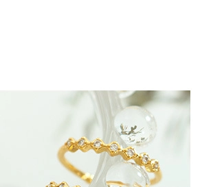 Macro shot of gold-plated daisy flower rings with small inlaid diamonds on glass stand