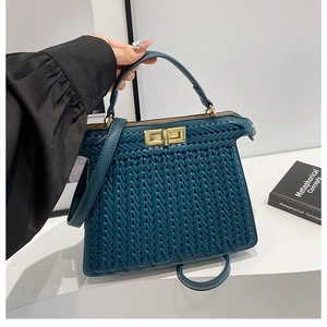 Detail of woven texture on teal handbag with golden clasp and leather handle