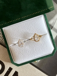 Close-up of pear-cut halo rings in silver and gold on a white leather jewelry box