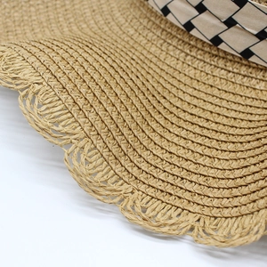 Close-up of woven straw sun hat with wavy edges and geometric patterned ribbon