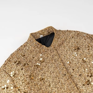 Dettaglio ravvicinato del tessuto tweed dorato con paillettes e collo a lupetto