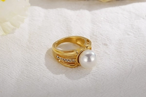 Detailed view of a wide gold ring with a large white pearl and zircon accents on textured fabric