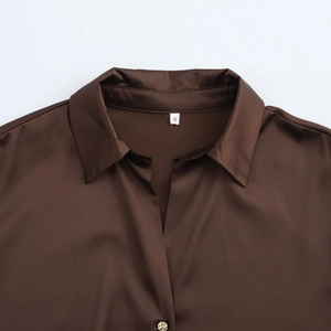 Detail of a brown satin shirt showing the lapel collar and a textured golden button