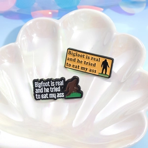 Creatively designed Bigfoot and gorilla enamel pins displayed on a pearl shell tray