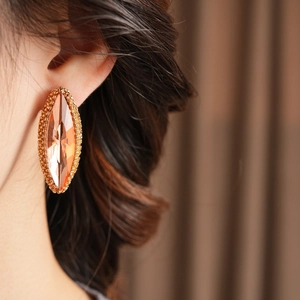 Close-up of marquise-cut amber stone earrings with golden beaded edging on a model