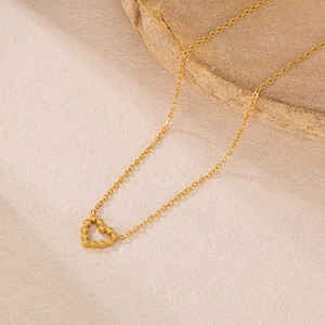 Détail d'un collier doré avec pendentif cœur en perles posé sur une pierre naturelle