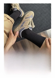 Close-up of black ribbed cotton crew socks worn with khaki mesh sneakers on a dark mat