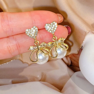 Detail of heart stud earrings with rhinestone bow and white pearl in golden wire frame