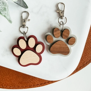 Handcrafted wooden paw print keychains with metal lobster clasps on marble surface