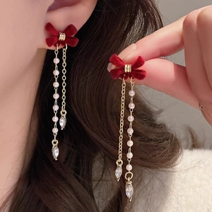 Close-up of long tassel earrings with red flocked bows and pearl chain details