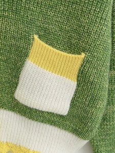Close-up of green knit sweater showing pocket detail and three-color textured stitching