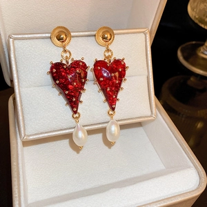 Vue macro détaillée de boucles d'oreilles cœur en résine rouge avec perles dorées et gouttes