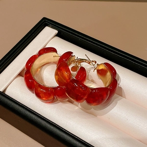Detail of red resin C-shaped earrings with gold metal posts in a gift box