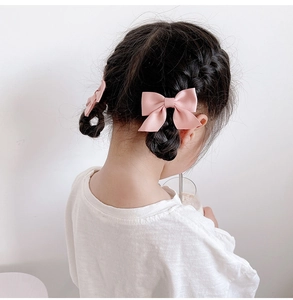 Detailed view of pink satin bow hair clips styled on braided pigtails for young girls