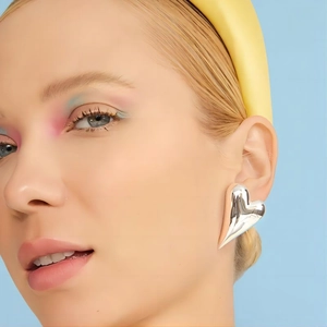 Polished heart-shaped silver earrings on model with blue background and yellow headband