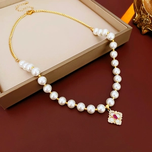 Detail of gold clover necklace with white pearls and red gem in a premium gift box