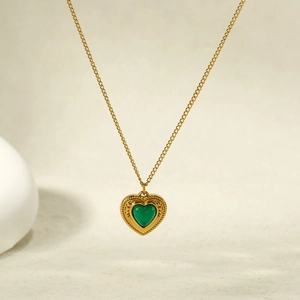 Vintage gold heart necklace with green gemstone pendant on a minimalist textured background