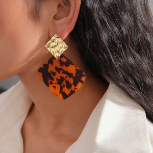 Close-up of tortoiseshell resin earrings with hammered gold metal on a model