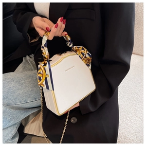 Close-up of white geometric handbag with gold frame and decorative silk scarf handle