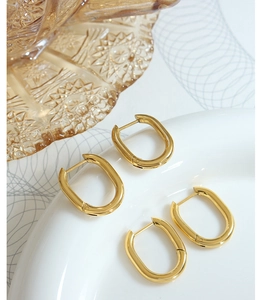 Macro view of polished 18K gold plated U-shaped geometric hoop earrings on a ceramic dish