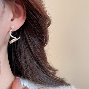 Macro detail of wave-shaped gold earrings with paved diamonds and a single white pearl