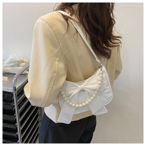 Chic white pleated fabric bag with bow and pearl chain worn by model in beige suit