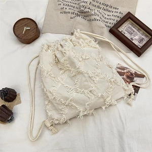 Close-up of beige canvas bucket bag featuring fringe tassels and drawstring cord closure