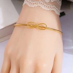Detail view of gold infinity knot bracelet worn with elegant white lace sleeves