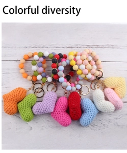 Colorful silicone bead wristlet keychains with woven heart charms on white wood background