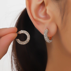 Detailed close-up of a C-shaped gold earring with full crystal rhinestones on an ear