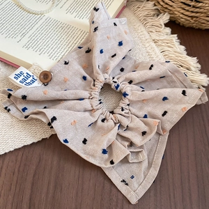 Detailed close-up of beige pleated fabric scrunchie with colorful embroidery and button