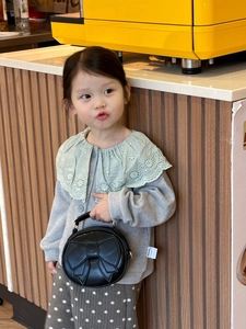 Detail of a black quilted round handbag with a bow decoration held by a child