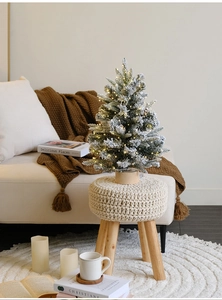 Close-up of a tabletop snow-flocked Christmas tree with warm LED lights on a wooden stool