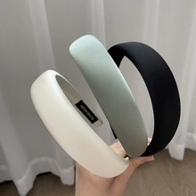 Close-up of white, light green, and black silk satin padded headbands held by hand