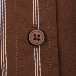 Macro view of a brown four-hole button on the striped fabric of a long sleeve shirt