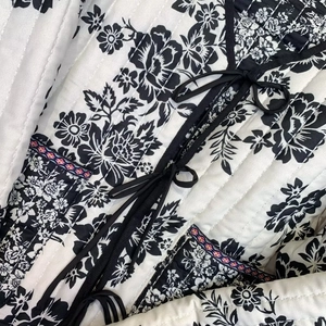Detail of quilted jacket featuring black and white floral prints and decorative bow tie