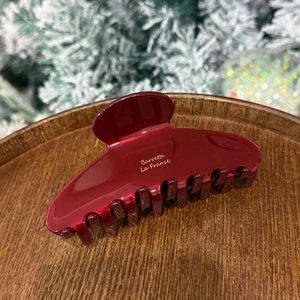 Close-up of burgundy acetate hair claw clip with gold lettering on a wooden tray