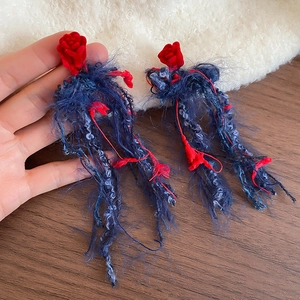 Dettaglio degli orecchini con rose di velluto rosso e lunghe nappe di colore blu scuro