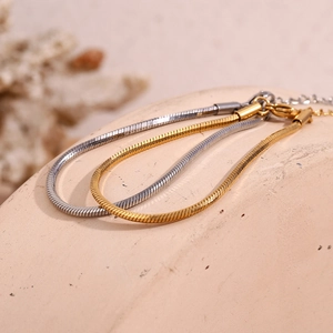 Macro shot of minimalist gold and silver hexagonal snake chains on textured stone