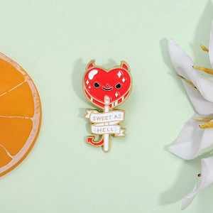 Close-up of heart lollipop enamel pin with devil horns and Sweet As Hell text