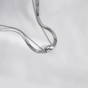 Detail of layered silver snake chain necklace with a polished cylindrical pendant