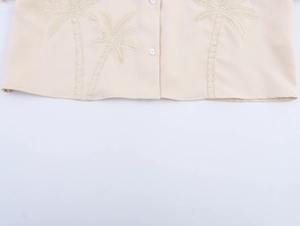 Detail of summer beige shirt hem featuring coconut tree embroidery and cotton linen texture