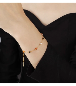 Detail of a thin gold necklace with multicolored circular beads on a model wearing black clothing