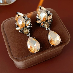 Macro detail of vintage water drop earrings with amber crystals on a velvet box