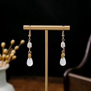 Detailed shot of golden floral hollow earrings with pearls on a T-shaped display stand