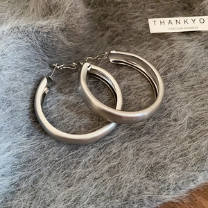 Detail of silver-gray brushed metal hoop earrings on soft plush background texture