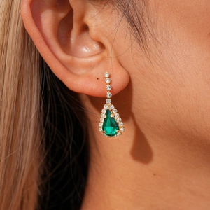 Close-up of elegant gold drop earrings with pear-cut green stones and sparkling cubic zirconia