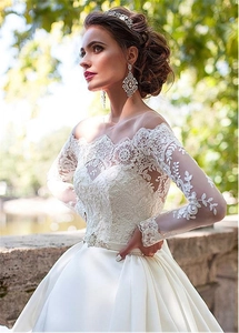 Close-up of elegant off-shoulder long sleeve bridal gown with lace and sequin belt