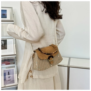 Detail of hand-woven straw bag featuring a bamboo handle and brown leather flap